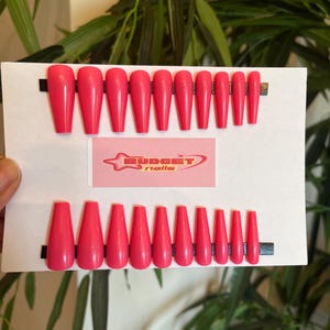 May include: A set of 10 pink coffin-shaped press-on nails. The nails are arranged in two rows on a white background. The nails are all the same size and shape. The nails are a bright, vibrant pink color. The text "BUDGET nails" is visible in the image.
