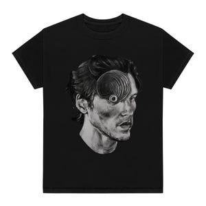 May include: Black t-shirt with a graphic of a man's face with a spiral design over one eye.