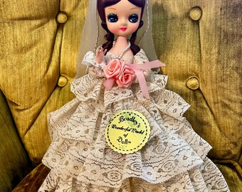 May include: Vintage bride doll with large blue eyes, wearing a white lace dress and veil. The doll has a pink rose bouquet and a pearl necklace. A tag reads "Bradley's Wonderful World of Dolls."