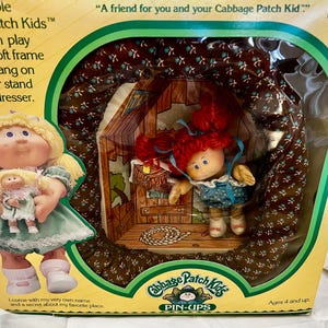 May include: Collectible Cabbage Patch Kids Pin-Ups doll in its original packaging. The box features a doll holding a smaller doll, and a doll inside a house-shaped display. The text on the box reads "A friend for you and your Cabbage Patch Kid."