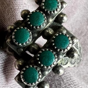 May include: Silver-toned earrings with a geometric design. Each earring features five round, dark green stones set in a scalloped bezel. The earrings have a vintage or antique aesthetic, with small silver ball accents.