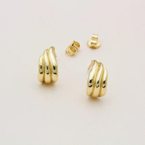 May include: A pair of gold-toned earrings with a wavy, ridged design. The earrings are small and delicate.