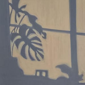 Op de afbeelding: Een schilderij van een raam met een lichtbeige achtergrond en een donkerblauwe lijst. Het raam toont een silhouet van een monstera-plant. De bladeren zijn lichtbeige en contrasteren met de donkerblauwe lijst en achtergrond.