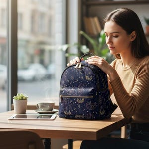 Könnte beinhalten: Marineblauer Rucksack mit goldenem Himmelsdesign. Der Rucksack hat einen oberen Griff, eine Fronttasche mit Reißverschluss und goldene Reißverschlüsse. Das Design umfasst Sterne, Monde und andere Himmelsymbole. Der Rucksack steht auf einem Holztisch.
