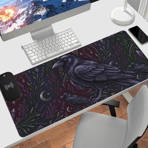 May include: A rectangular desk mat with a raven illustration, two smaller ravens, and botanical and celestial designs on a dark background. Includes a wireless charging pad. The mat is designed for a desk.