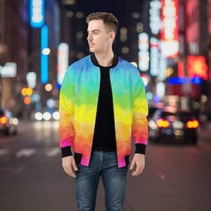 May include: A rainbow-colored bomber jacket with black trim and a black shirt. The jacket features a watercolor design with shades of blue, yellow, orange, and pink. The person is wearing blue jeans and white sneakers.