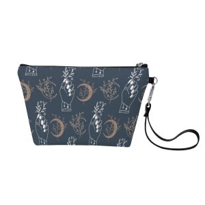 May include: A dark blue zippered makeup bag with a white and gold pattern of hands holding crescent moons and floral sprigs.