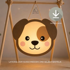 May include: A paper lantern craft template featuring a dog face with brown ears, a tan patch over one eye, pink cheeks, and a black nose. The design includes the text pirka, a download icon, and the German text LATERNE ZUM AUSSCHNEIDEN UND SELBER BASTELN.