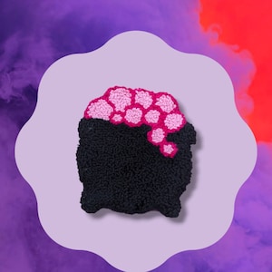 May include: A black cauldron with a pink and white flower design on top. The cauldron is made of yarn and is a handmade craft.