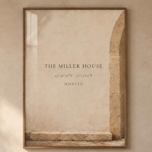 May include: A rectangular wall art print in a thin wooden frame featuring a beige stone archway, the text THE MILLER HOUSE, coordinates, and the Roman numeral MMXVIII. The print is displayed above a beige sofa with cushions and a wooden coffee table.