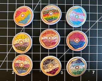 May include: Nine round pinback buttons with different designs of donuts with sprinkles and frosting in various colors, including pink, blue, yellow, green, and purple.