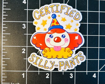 May include: A white sticker with a cartoon clown wearing a red and blue hat with yellow stars. The text "CERTIFIED SILLY-PANTS" is written in a yellow, blue, and red font.