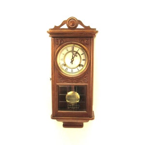 May include: A wooden wall clock with a pendulum and Roman numeral markings on the face. The clock has a dark brown finish and a glass front.