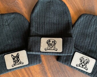 May include: Three black knit beanies with a brown leather patch featuring a dog's face on each beanie.