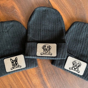 May include: Three black knit beanies with a brown leather patch featuring a dog's face on each beanie.
