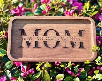 May include: A wooden tray with the words "MOM You are the piece that holds this family together." engraved on it. The tray is sitting on a bed of pink flowers.