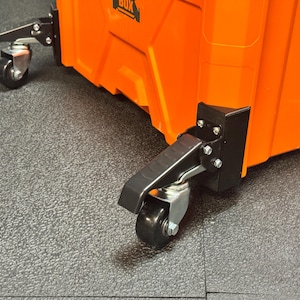 May include: A bright orange storage box featuring two black swivel caster wheels with integrated locking levers attached to the base. The wheels are made of black plastic and metal, and the box displays a partial black logo reading BOX.