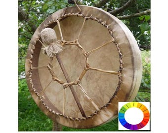 May include: A brown leather drum with a wooden frame and a woven design. The drum is hanging from a tree branch and has a small, brown, fabric-covered mallet attached to it.