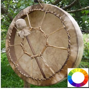 May include: A brown leather drum with a woven design and a wooden stick with a fabric head. The drum is hanging from a tree branch.