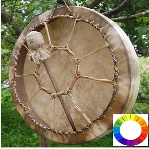 May include: A brown leather drum with a woven design and a wooden stick with a fabric head. The drum is hanging from a tree branch.