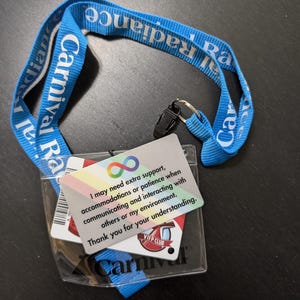 May include: A blue lanyard with the text "Carnival Radiance" printed on it. A clear plastic badge holder with a white card that reads "I may need extra support, accommodations or patience when communicating and interacting with others or my environment. Thank you for your understanding." and a red card with the text "VIP Club Carnival" is attached to the lanyard.