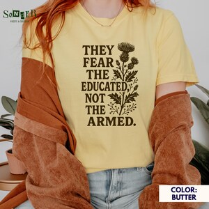 May include: A yellow t-shirt with a brown graphic print of a floral design and the text "They fear the educated, not the armed."