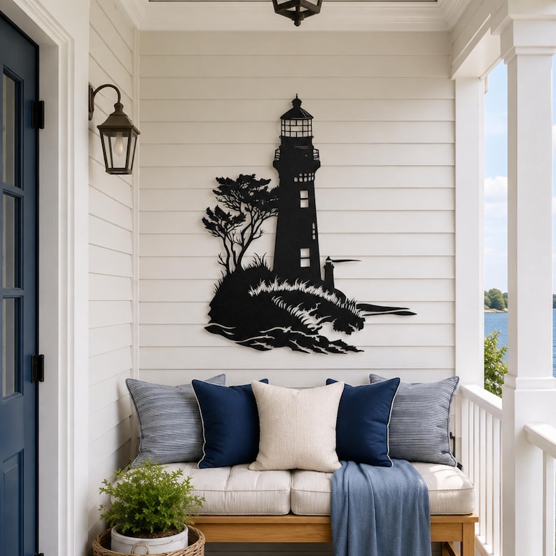 May include: A black metal wall art piece featuring a lighthouse silhouette standing on a rocky shore with a tree, crashing waves, and a smaller secondary lighthouse structure, mounted on a horizontal white paneled wall surface.