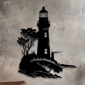 May include: A black metal wall art piece featuring a silhouette of a lighthouse standing on a rocky cliffside with a tree, crashing waves at the base, and a small secondary structure extending to the right side of the main lighthouse tower.
