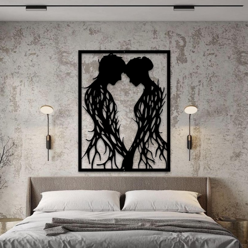 May include: Black metal wall art depicting two figures in silhouette, their bodies intertwined with a tree-like design. The figures are facing each other, holding hands, within a rectangular frame. The artwork is mounted above a bed.