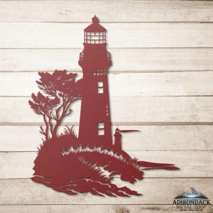 May include: A dark red metal wall art piece featuring a lighthouse silhouette standing on a rocky base with a tree and crashing waves. The design includes a smaller secondary lighthouse structure and the text Adirondack Metal Shop Metal Wall Decor.