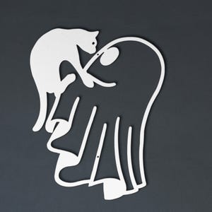 May include: A white metal wall art piece featuring a continuous line silhouette of a cat perched atop a ghost figure. The design is minimalist and flat, showcasing the cat's arched back and the ghost's flowing, draped form in a single cutout shape.