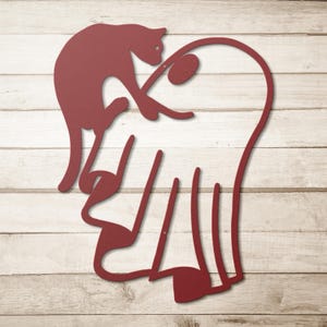 May include: A dark red metal wall art piece featuring a stylised silhouette of a cat perched atop a large heart shape. The design is composed of continuous lines forming the feline figure and the heart outline, creating a flat, cutout aesthetic.
