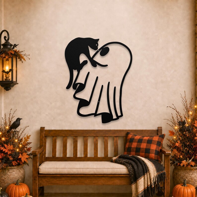 May include: A black metal wall art piece featuring a silhouette of a cat perched on top of a ghost. The design is minimalist with clean lines, depicting the cat with its tail curved and the ghost with a draped, flowing sheet appearance.