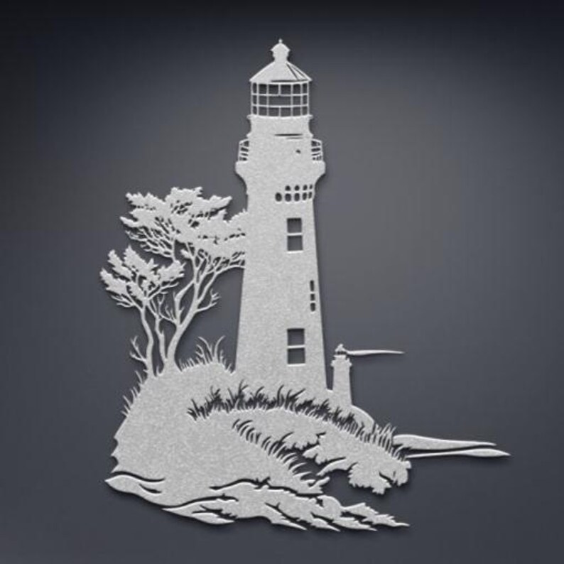 May include: A silver-coloured metal wall art piece featuring a detailed silhouette of a lighthouse standing on a rocky cliffside with a tree and crashing waves at the base. The design includes cutouts for the lantern room and windows.