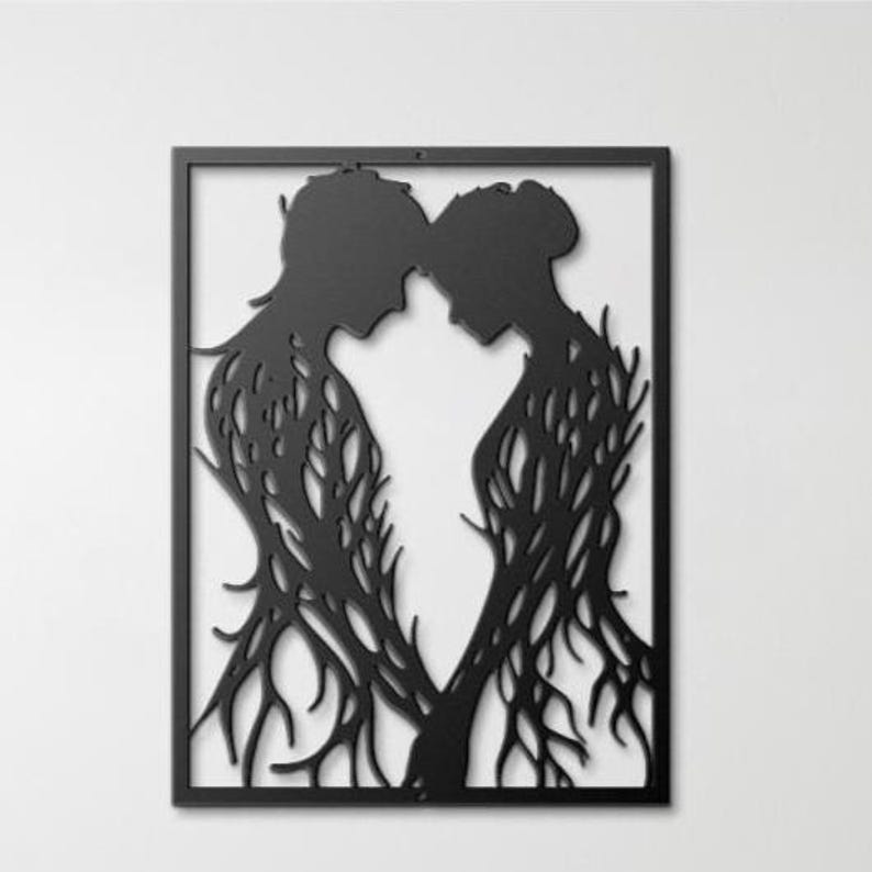 May include: Black metal wall art featuring two silhouetted figures in an embrace, their bodies intertwined with a tree-like design. The artwork is framed in a black rectangular border, creating a striking contrast against the white background.