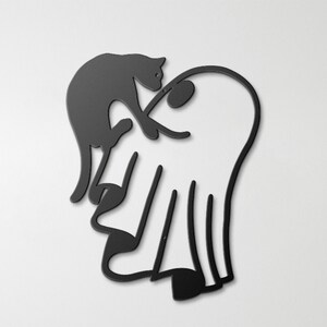 May include: A black metal wall art piece featuring a silhouette of a cat perched on top of a ghost. The design is composed of clean, continuous lines forming the shapes of the feline and the draped figure, creating a flat, minimalist aesthetic.