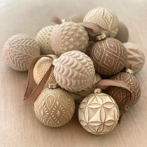 Pu&ograve; includere: Una collezione di addobbi natalizi color crema con vari motivi in rilievo. Gli addobbi sono in ceramica e hanno uno stile rustico e da fattoria.