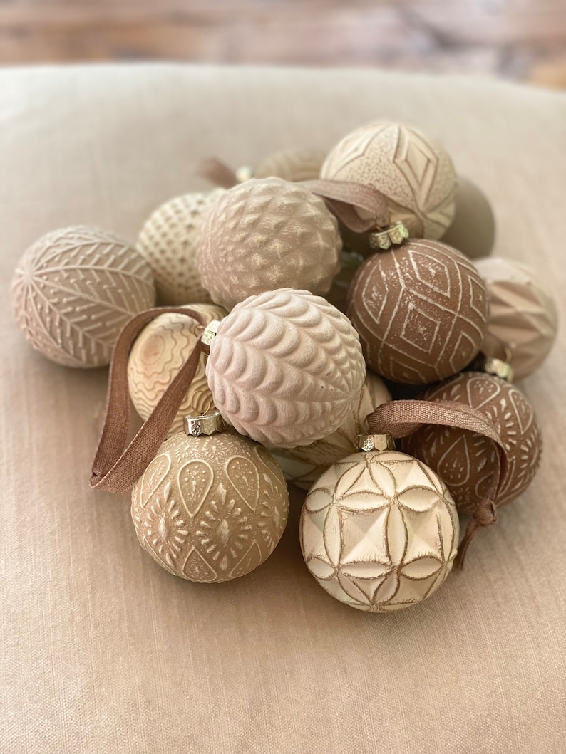 Pu&ograve; includere: Una collezione di addobbi natalizi color crema con vari motivi in rilievo. Gli addobbi sono in ceramica e hanno uno stile rustico e da fattoria.