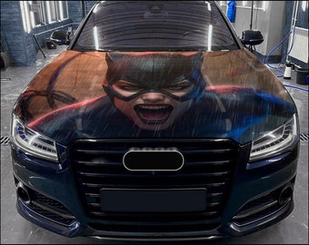 Può includere: Un'auto nera con un'avvolgente personalizzata per il cofano che presenta il viso di una donna con una maschera da gatto. L'avvolgente ha uno schema di colori rosso e blu scuro con un effetto pioggia.