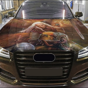 May include: A black car with a custom hood wrap featuring a fantasy illustration of a warrior with a sword and a monster. The illustration is in shades of brown, gold, and green.