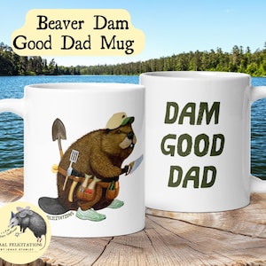 May include: Two white ceramic mugs featuring a brown beaver illustration wearing a tan cap, green sneakers, and a tool belt with a shovel and spatula. The text on the mugs reads DAM GOOD DAD in dark green letters, with Beaver Dam Good Dad Mug above.