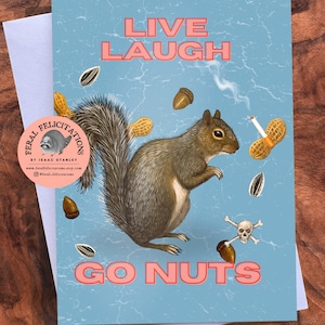May include: Greeting card with a squirrel illustration. The card has the words "LIVE LAUGH GO NUTS" in pink text. The squirrel is surrounded by peanuts, acorns, and sunflower seeds. A skull and crossbones is also present.