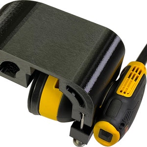 Puede incluir: Un soporte de lijadora impreso en 3D negro con una lijadora eléctrica amarilla y negra unida. La lijadora tiene un cable negro y un gatillo amarillo.