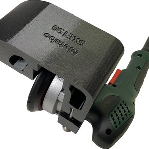 Könnte beinhalten: Ein schwarzer 3D-gedruckter Werkzeugaufsatz für eine Bohrmaschine. Der Aufsatz hat eine runde Schleifscheibe und den Text "METABO SXE150" aufgedruckt. Die Bohrmaschine ist grün und schwarz mit einem roten Knopf.