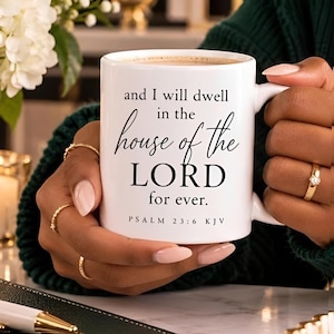 Puede incluir: Una taza de cerámica blanca con texto impreso en negro que dice, and I will dwell in the house of the LORD for ever. PSALM 23:6 KJV. La taza tiene un acabado liso, un asa curva y contiene un líquido de color marrón claro hasta el borde.