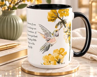 Puede incluir: Una taza de cerámica blanca con interior y asa negros, que presenta una ilustración en acuarela de un colibrí cerca de flores amarillas. El texto dice: However I am is always on the sweetness. A Hummingbird look everyday little blessings in the living life.