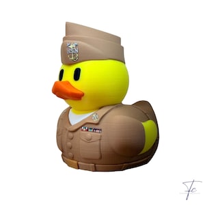 May include: A yellow rubber duck wearing a tan military-style uniform and a matching garrison cap. The cap features a USN anchor emblem, and the uniform includes a white shirt collar, a row of buttons, a chest pocket, and a colorful ribbon bar.