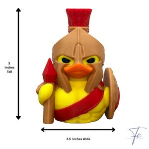 May include: A yellow duck figurine, 7.6 cm tall and 6.4 cm wide, styled as a Spartan warrior. It features a tan helmet, red sash, and holds a spear and shield. The duck has an orange beak and an angry expression.
