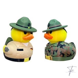 Könnte beinhalten: Zwei gelbe Gummienten in Militäruniformen. Eine Ente trägt eine beige Uniform und einen grünen Hut, die andere eine Tarnuniform und einen grünen Hut. Beide haben orangefarbene Schnäbel.