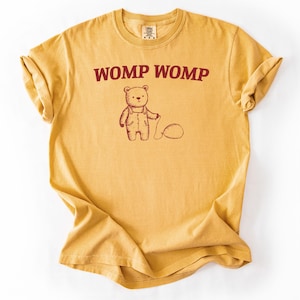 May include: A mustard yellow t-shirt with a cartoon bear wearing overalls and the text "WOMP WOMP" in red.